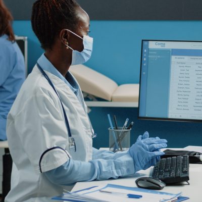 Black patient and doctor with face masks doing medical checkup in cabinet. African american medic doing healthcare consultation with person while protecting against coronavirus pandemic